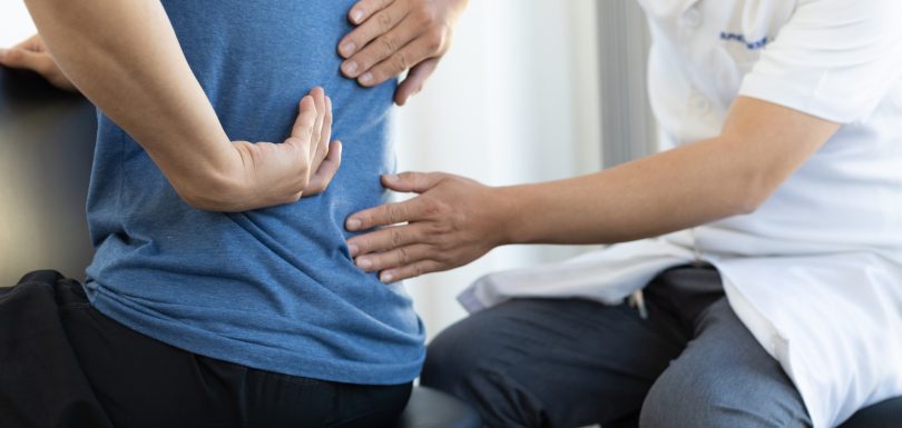 The doctor is diagnosing the patient's back pain. A male with back pain sees a doctor for treatment.